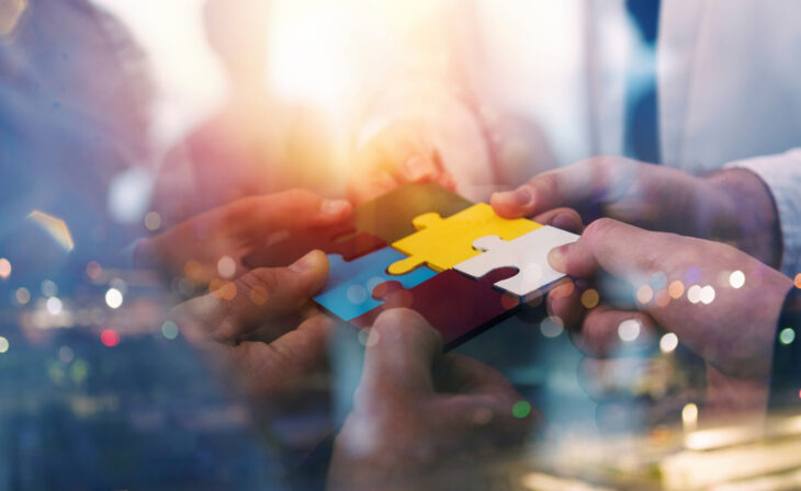 Business people join puzzle pieces in a modern office. Concept of teamwork and partnership. double exposure with light effects
